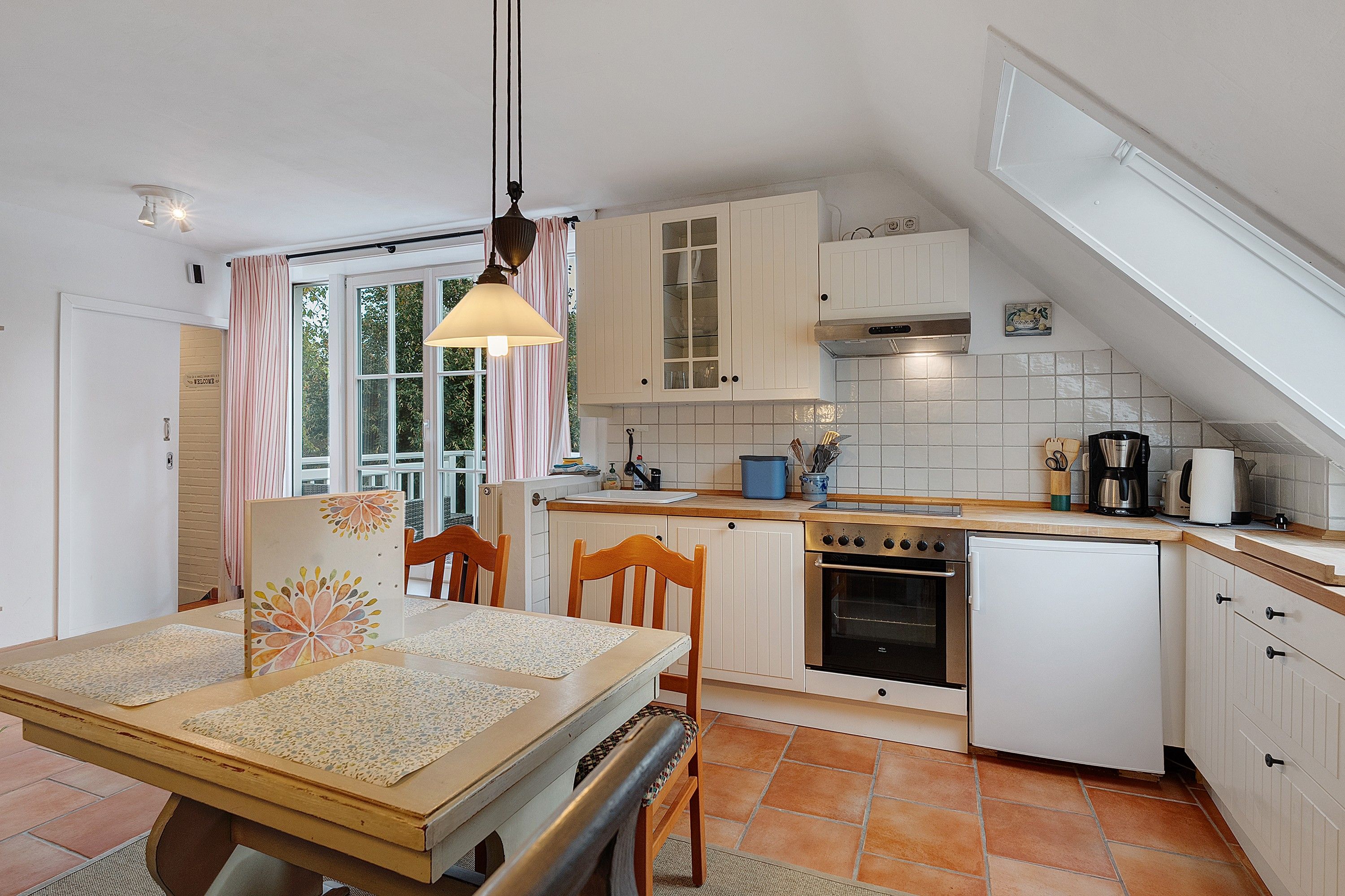 Een keuken met witte kastjes, een houten tafel en een hanglamp.