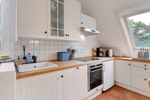 A kitchen with white cabinets, a double sink, a stove, and a window.