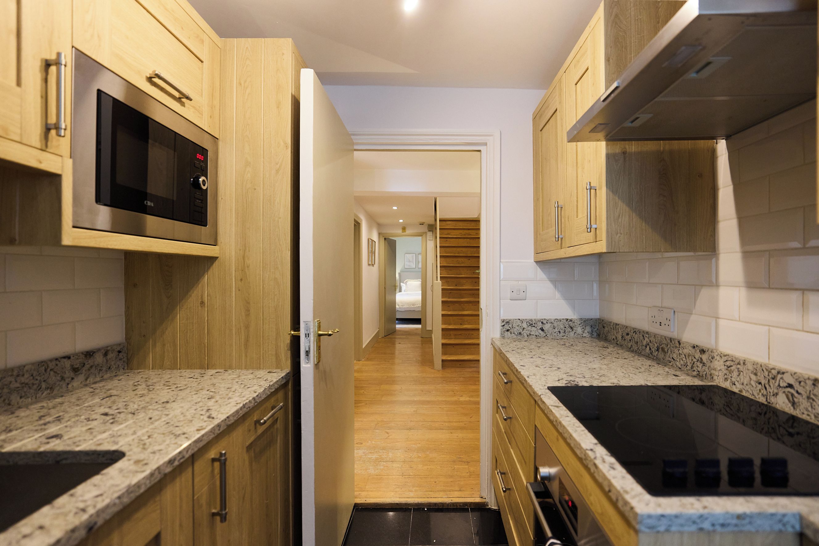 A narrow kitchen with wooden cabinets, a microwave, and a stove.