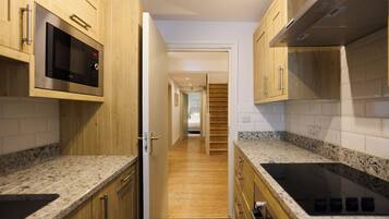 A narrow kitchen with wooden cabinets, a microwave, and a stove.