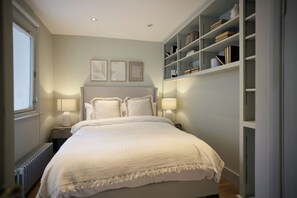 Ein Schlafzimmer mit einem Bett, Nachttischlampen, einem Heizkörper und einem Bücherregal.