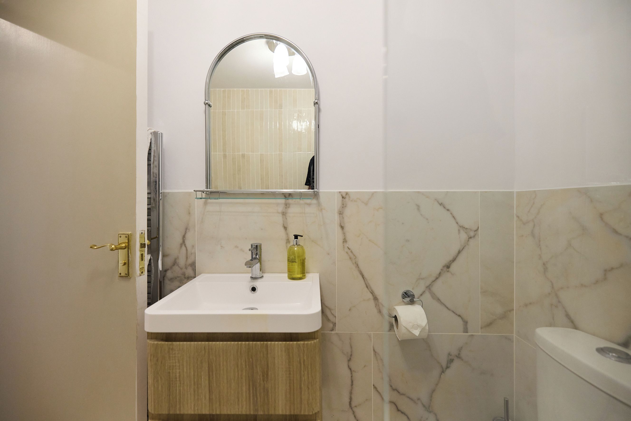 A bathroom with a white sink, a mirror, a toilet, and a bottle of hand soap.
