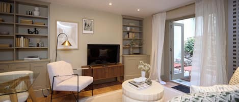 A modern living room with a flat-screen TV, a white armchair, a sofa, a coffee table, and a bookshelf.
