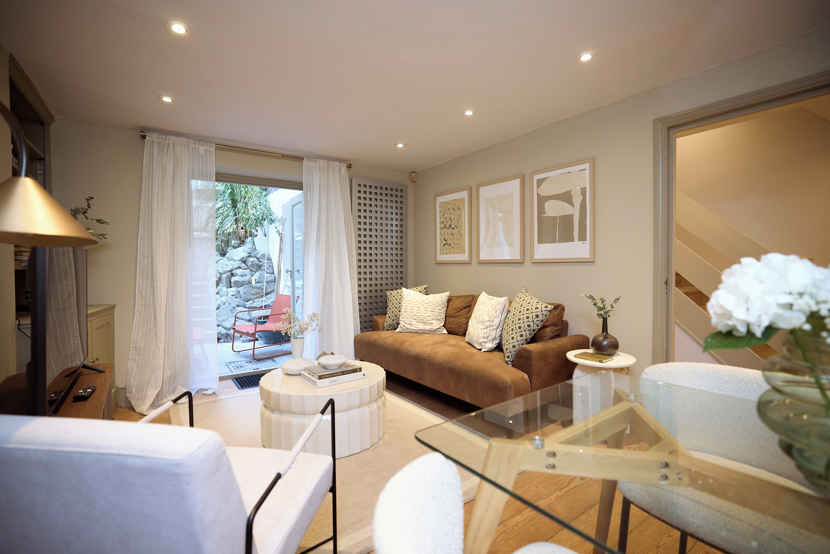 A modern living room with a glass coffee table, a brown sofa, and a white armchair.
