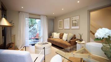 A modern living room with a glass coffee table, a brown sofa, and a white armchair.
