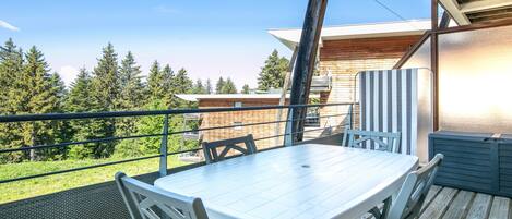 A wooden deck with a table and chairs, overlooking a forested area.
