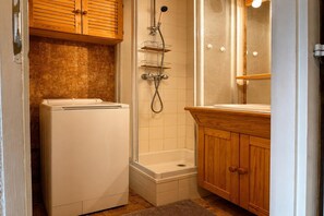 Ein kleines Badezimmer mit Waschmaschine, Dusche und Handbrause sowie ein Holzkosmetikschrank mit Spiegel.