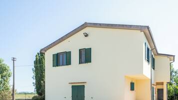 A two-story building with a flat roof, a green door, and two windows with shutters.