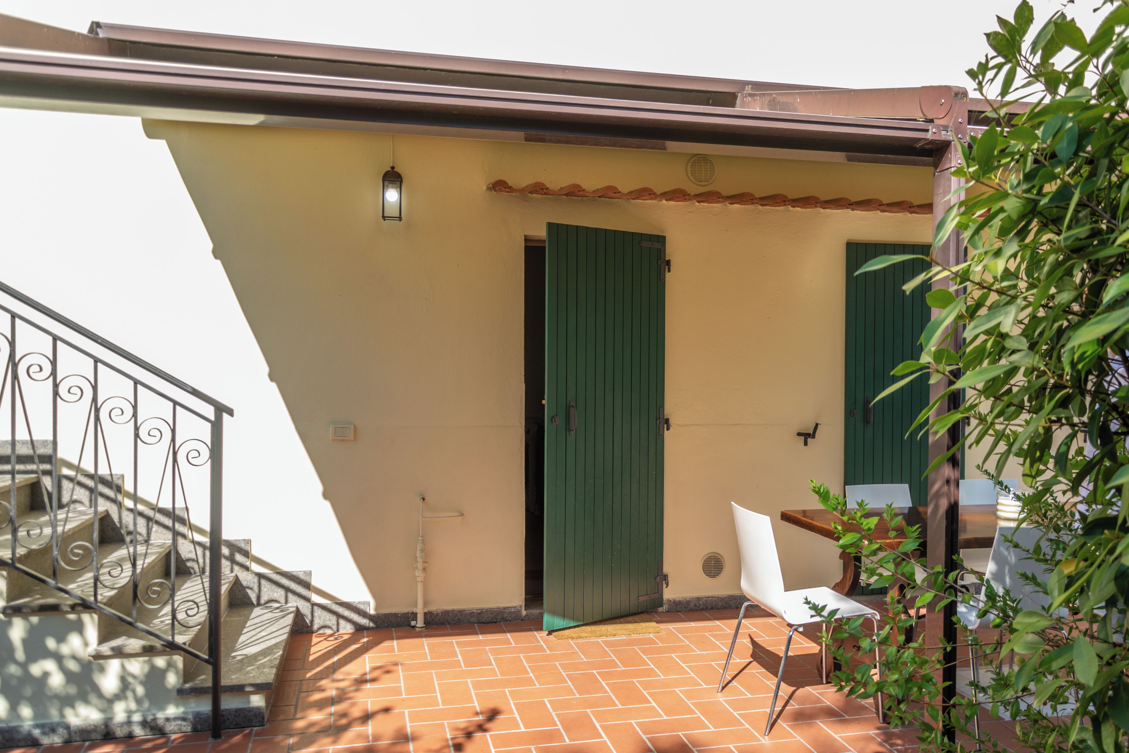 A terrace with a tiled floor, a green door, a white chair, and a metal railing.