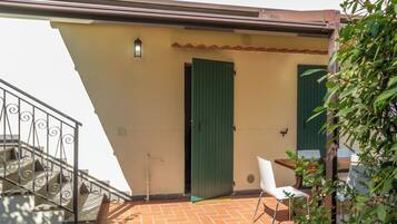 A terrace with a tiled floor, a green door, a white chair, and a metal railing.