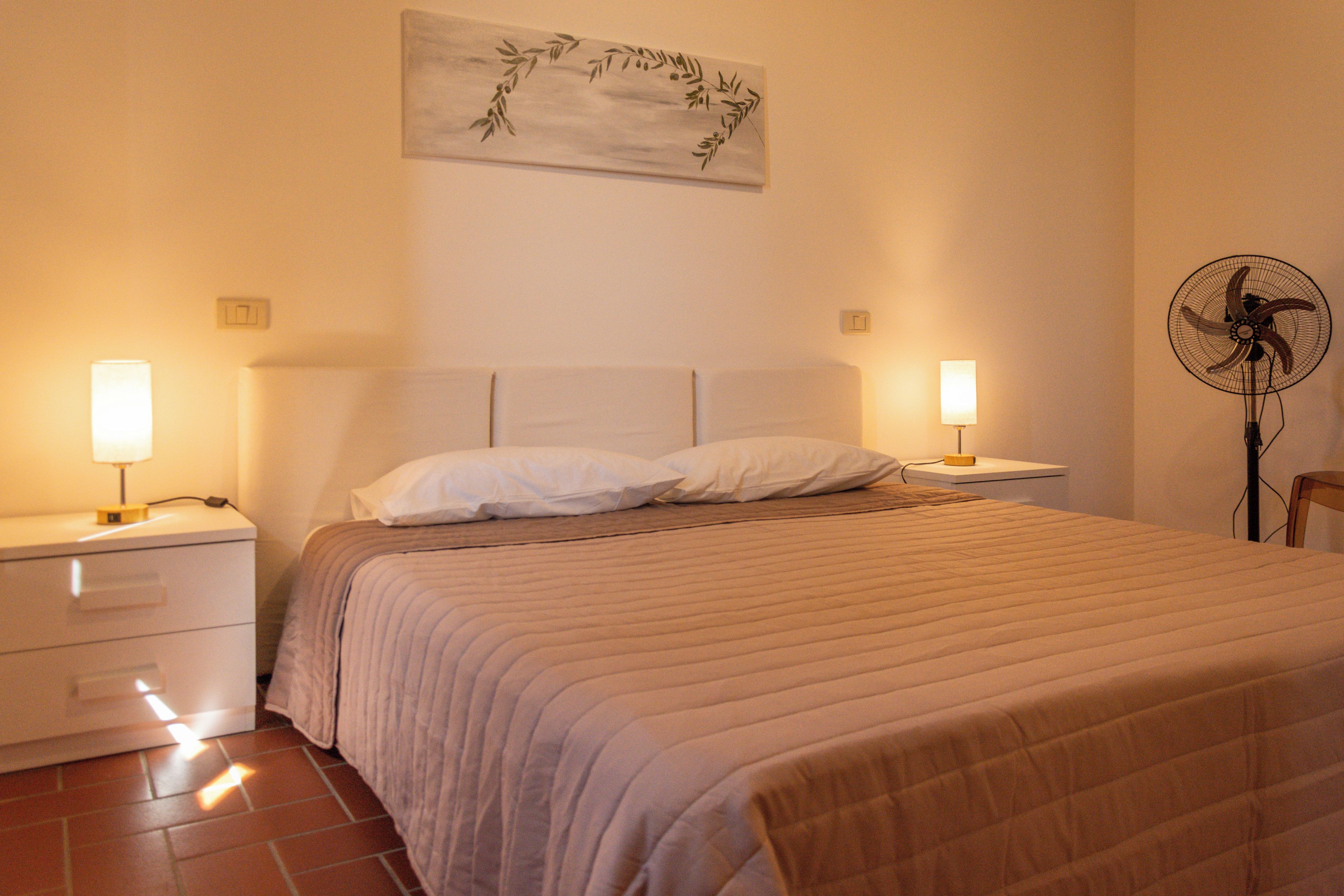 A neatly made bed with a headboard, two bedside tables with lamps, and a wall-mounted fan.