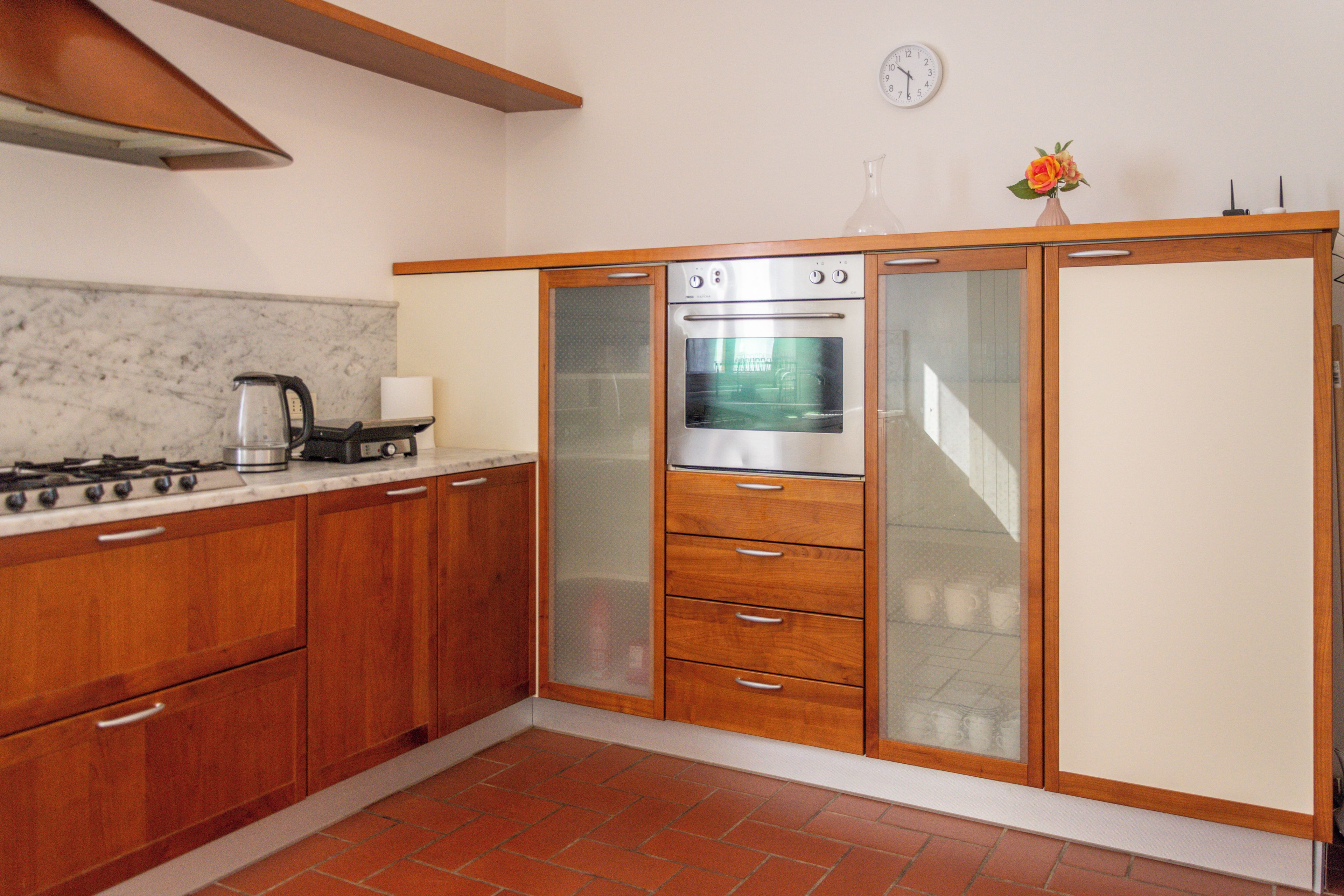 A kitchen with wooden cabinets, a built-in oven, a stove, and a clock on the wall.