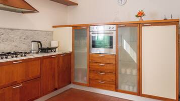 A kitchen with wooden cabinets, a built-in oven, a stove, and a clock on the wall.