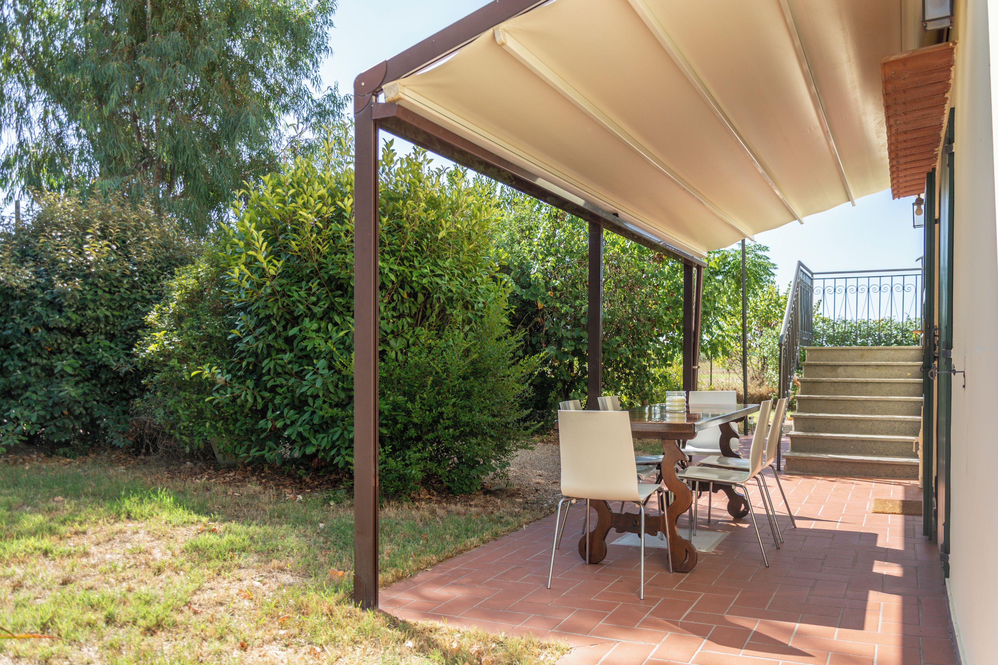 An outdoor patio with a table and chairs, a covered area with a roof, and a staircase leading to an upper level.