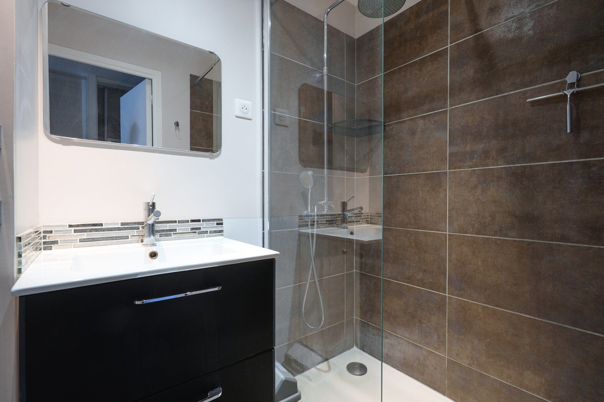 Un bagno moderno con doccia vetrata, un lavandino bianco e un mobile contenitore nero.