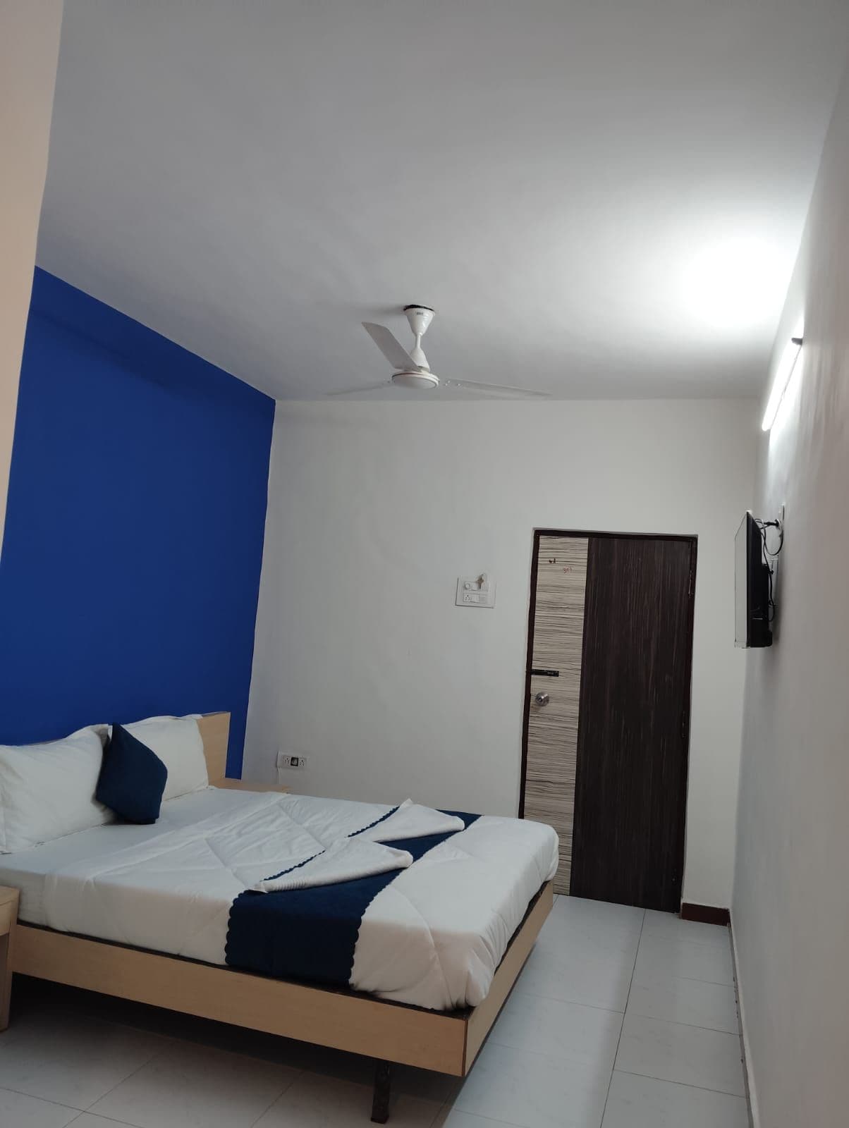 Ein Schlafzimmer mit einem Bett, einem Deckenventilator, einer Tür und einer wandmontierten Lampe.