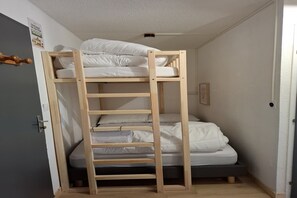 Ein Stockbett mit einer Holzleiter, weißer Bettwäsche und einer Tür mit Griff.