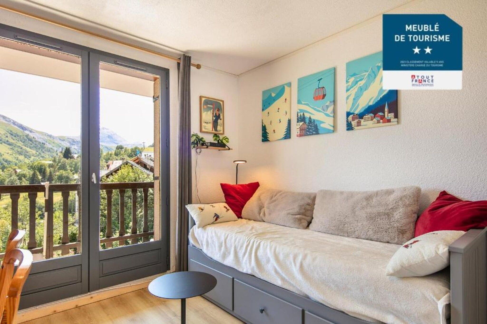 Habitación con cama, una silla, una mesa y vista al exterior. Hay cuadros en la pared y un cartel que indica una atracción turística.