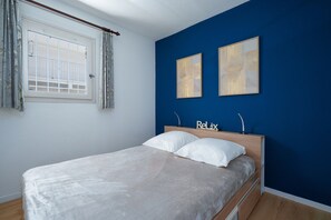 A bedroom with a bed, two wall-mounted artworks, a window with curtains, and a 'Relax' sign. - Family Apartment for 6 in Les Deux Alpes (Le Grau-du-Roi)