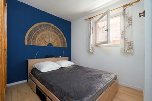 A bedroom with a bed, a wall-mounted decorative item, a window with curtains, and a wooden floor. - Family Apartment for 6 in Les Deux Alpes (Le Grau-du-Roi)