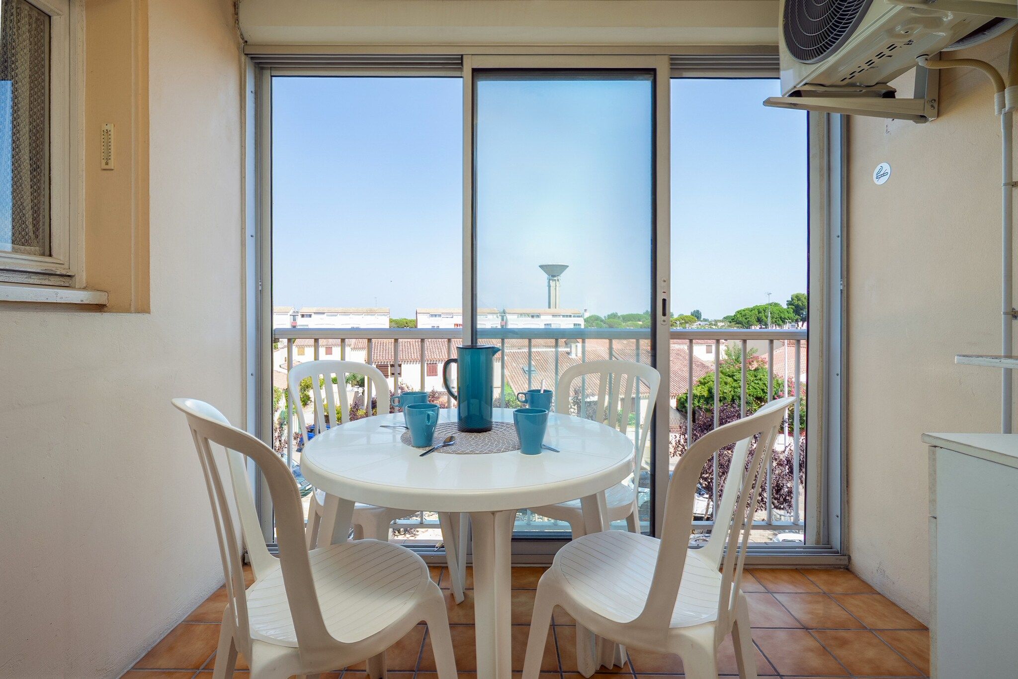 Un balcon avec une table et des chaises, une carafe d’eau et un ventilateur.