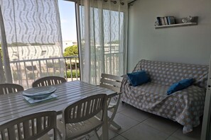 Een kamer met een eettafel, stoelen, een bank met gekleurde kussens en een boekenplank.