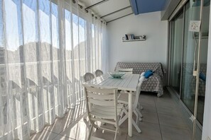 A balcony with a table and chairs, a sofa, and a glass door leading to a shower area. - Seafront Stay near South Beach (Le Grau-du-Roi)