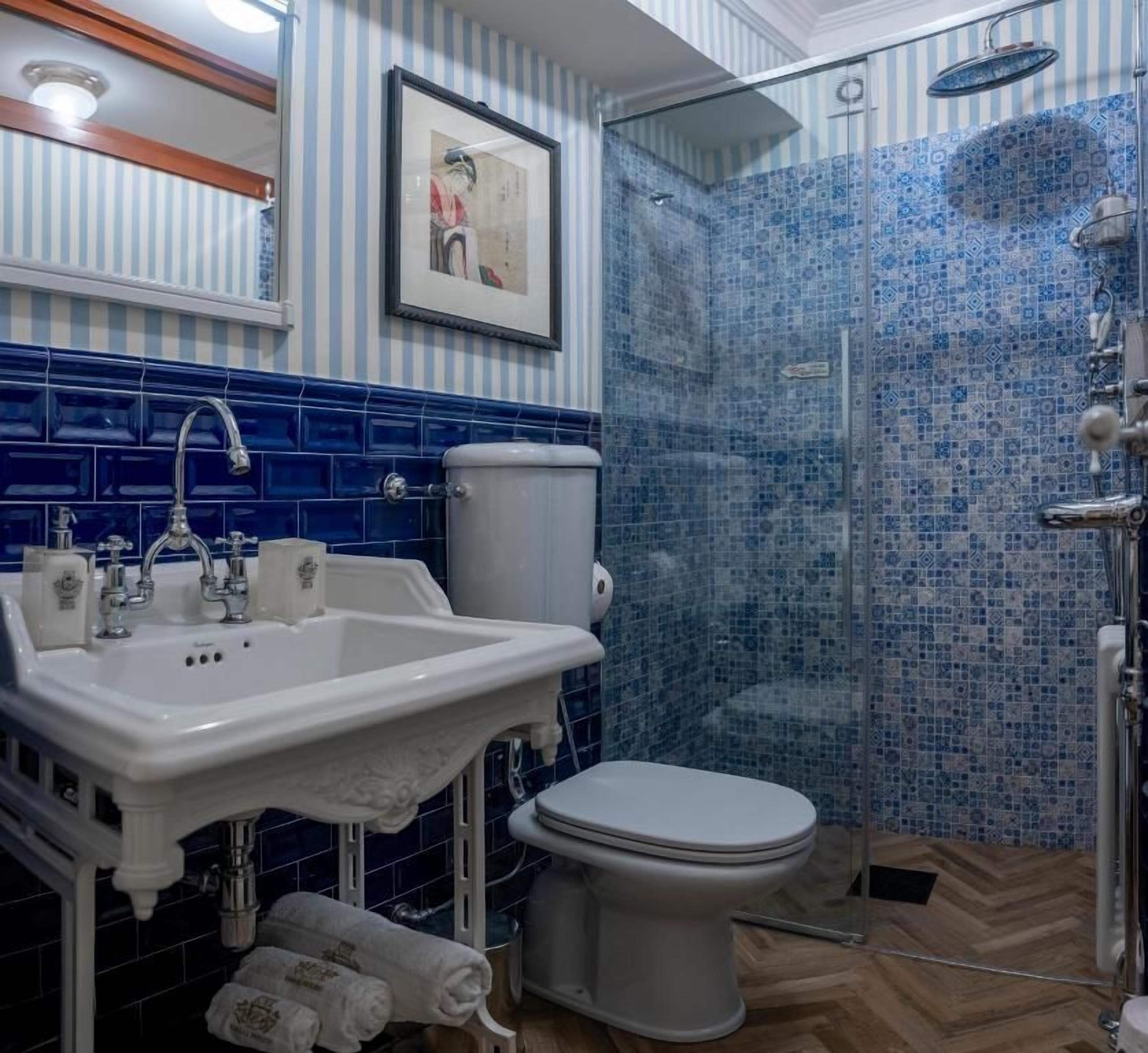 A bathroom with a white sink, a toilet, and a shower area with blue mosaic tiles.