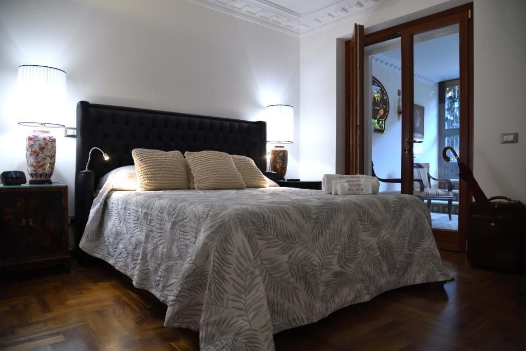 A bedroom with a large bed, two bedside lamps, a nightstand, and a door leading to another room.