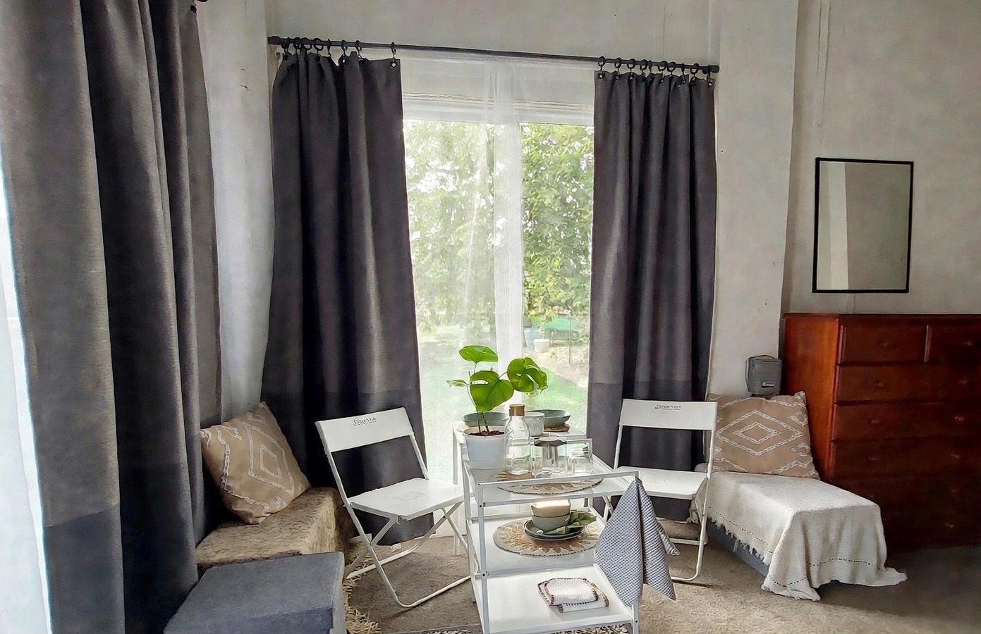 A room with a bed, a small table with a plant, and a window with curtains.