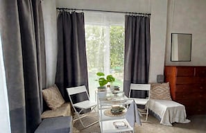 A room with a bed, a small table with a plant, and a window with curtains.