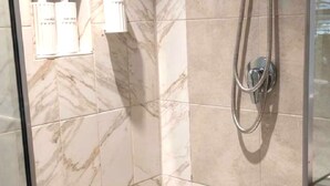 A bathroom with marble tiles, a shower with a hose, and a glass door. - Cozy 1-bedroom apartment in welcoming Cottesloe with AC (Cottesloe)