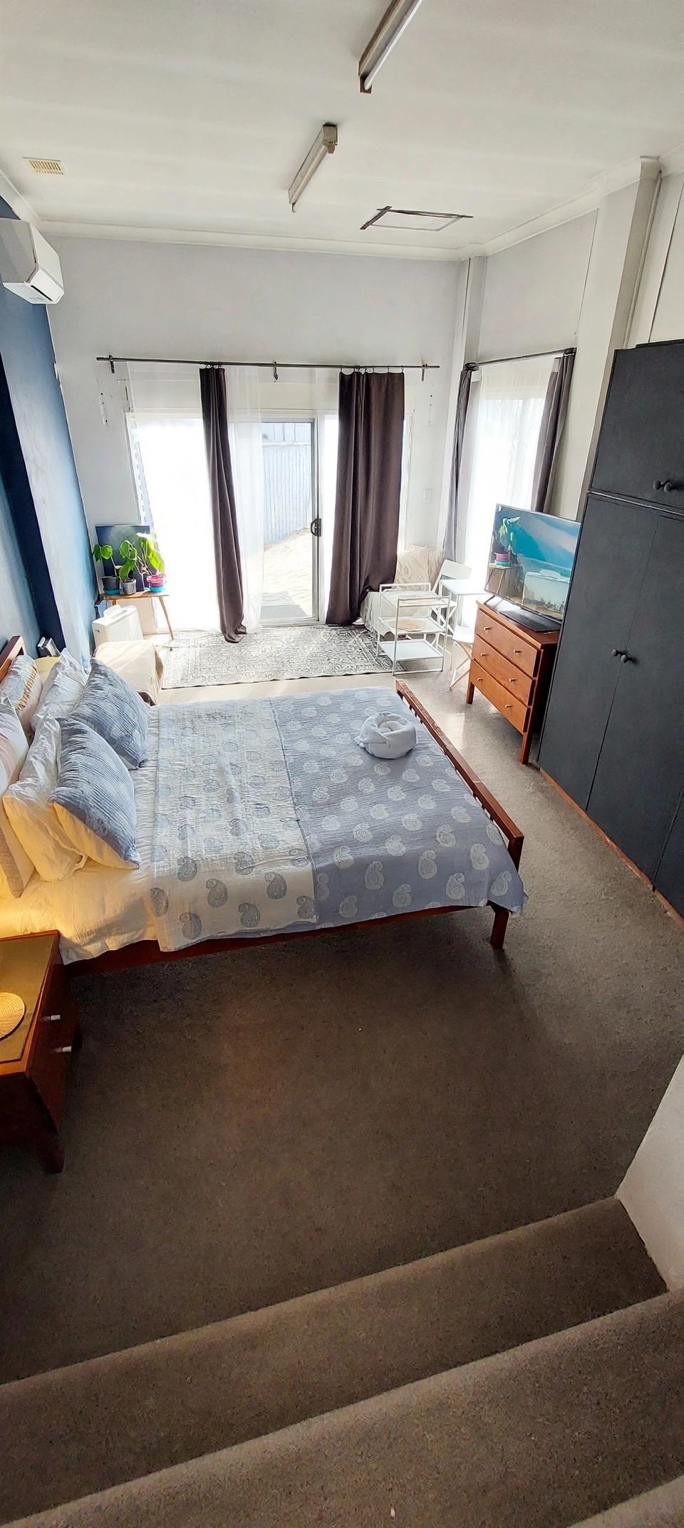 A bedroom with a bed, a dresser, a TV, and a window with curtains.