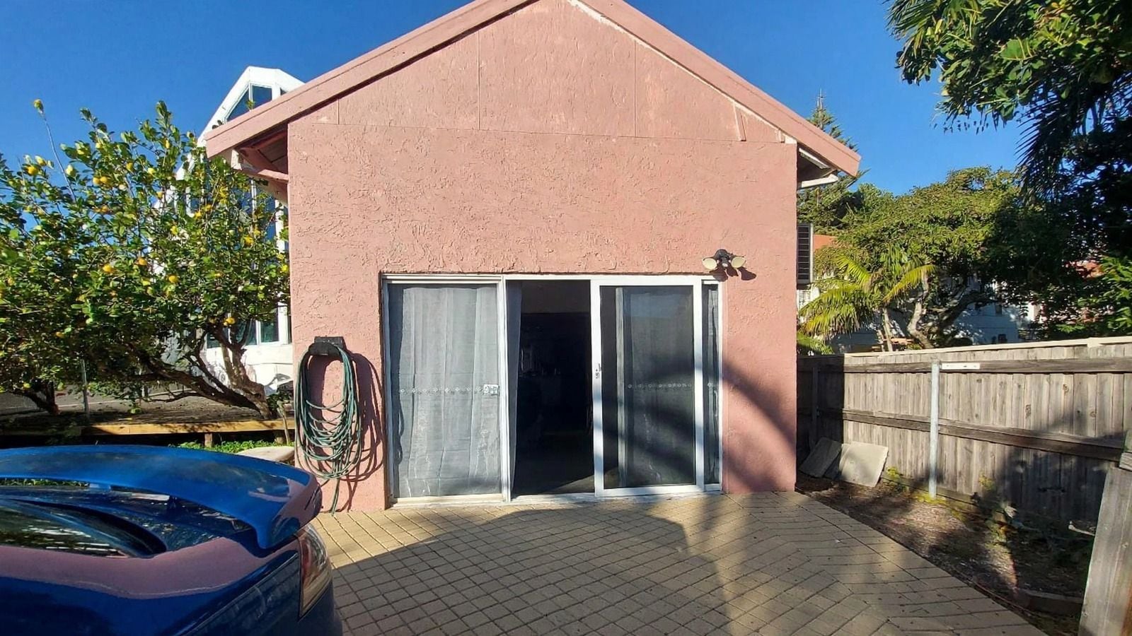 Un edificio residencial con una puerta de garaje, una manguera y un coche azul estacionado al frente.