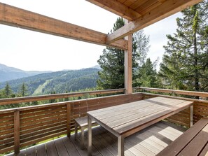 Une terrasse en bois avec une table et des bancs, offrant une vue sur une vallée boisée et des montagnes.