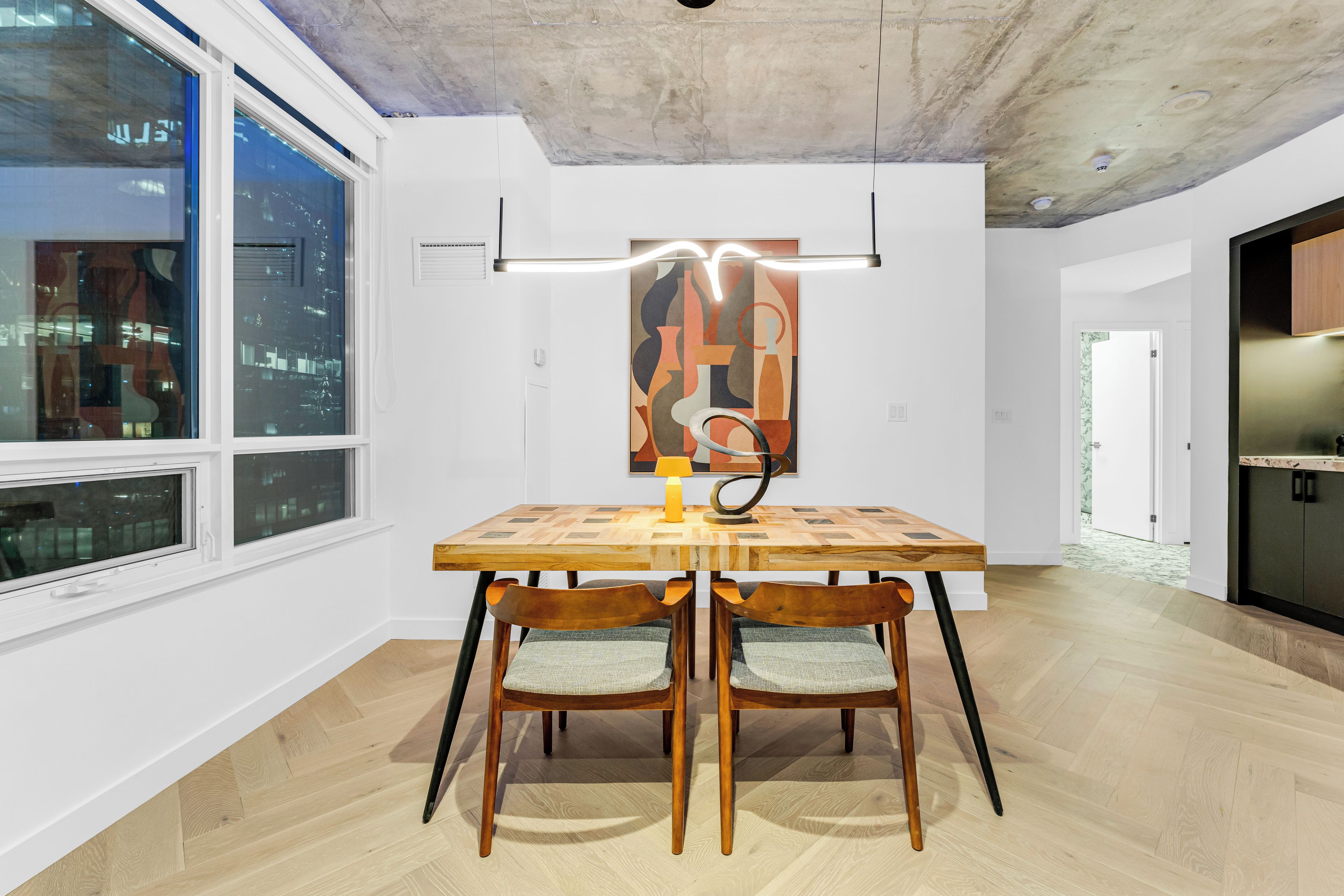 Un coin repas avec une table et des chaises en bois, un luminaire moderne et une vue sur le paysage urbain par la fenêtre.