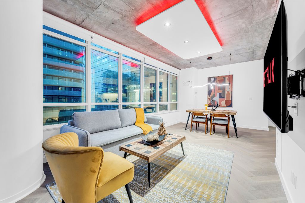 A modern living room with a sofa, armchair, coffee table, and a dining area with a table and chairs.