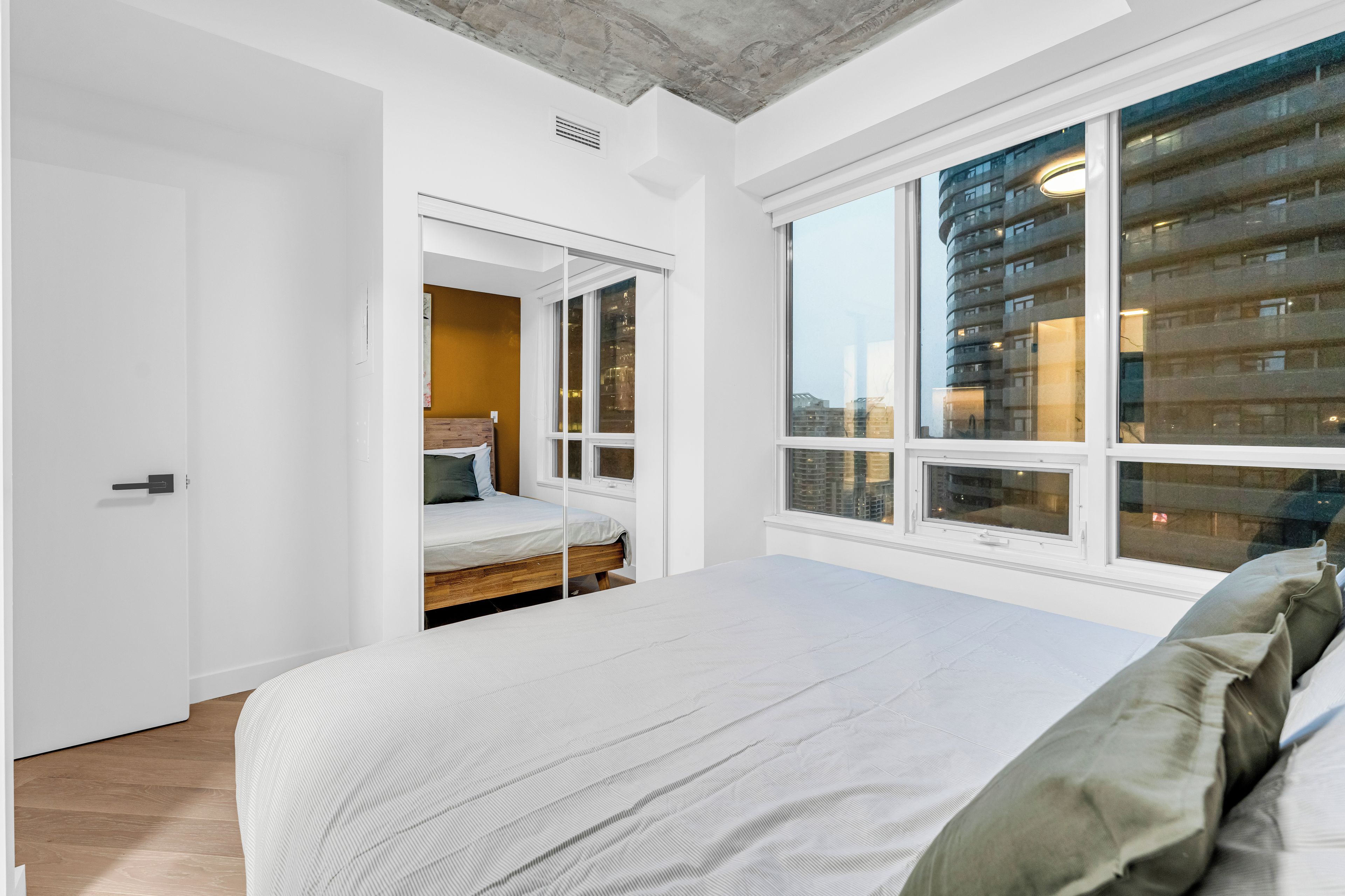 Une chambre avec un grand lit, une armoire et une fenêtre donnant sur la ville.