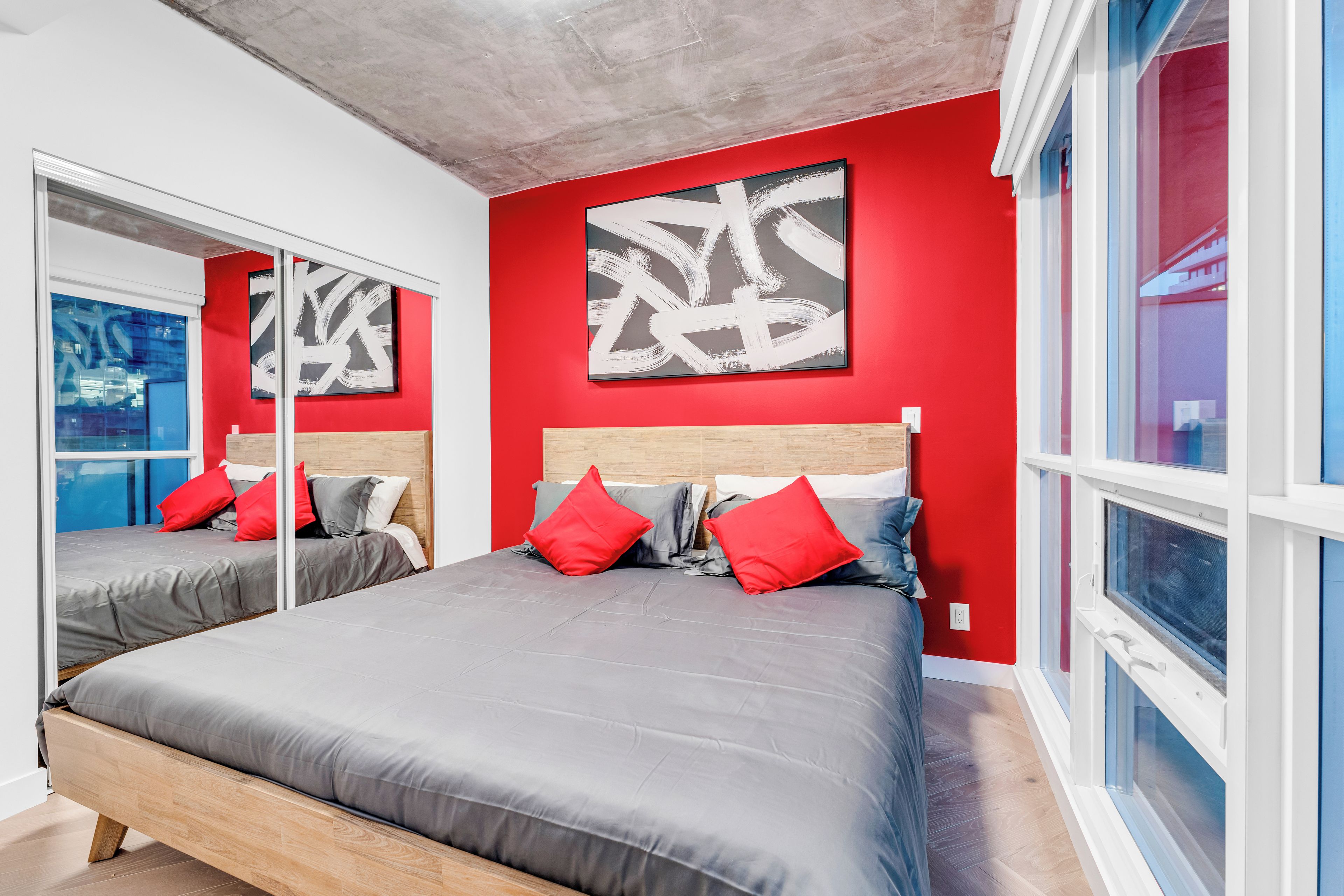 Une chambre moderne avec deux lits, des murs rouges et des œuvres d’art abstraites.