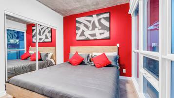 Une chambre moderne avec deux lits, des murs rouges et des œuvres d’art abstraites.