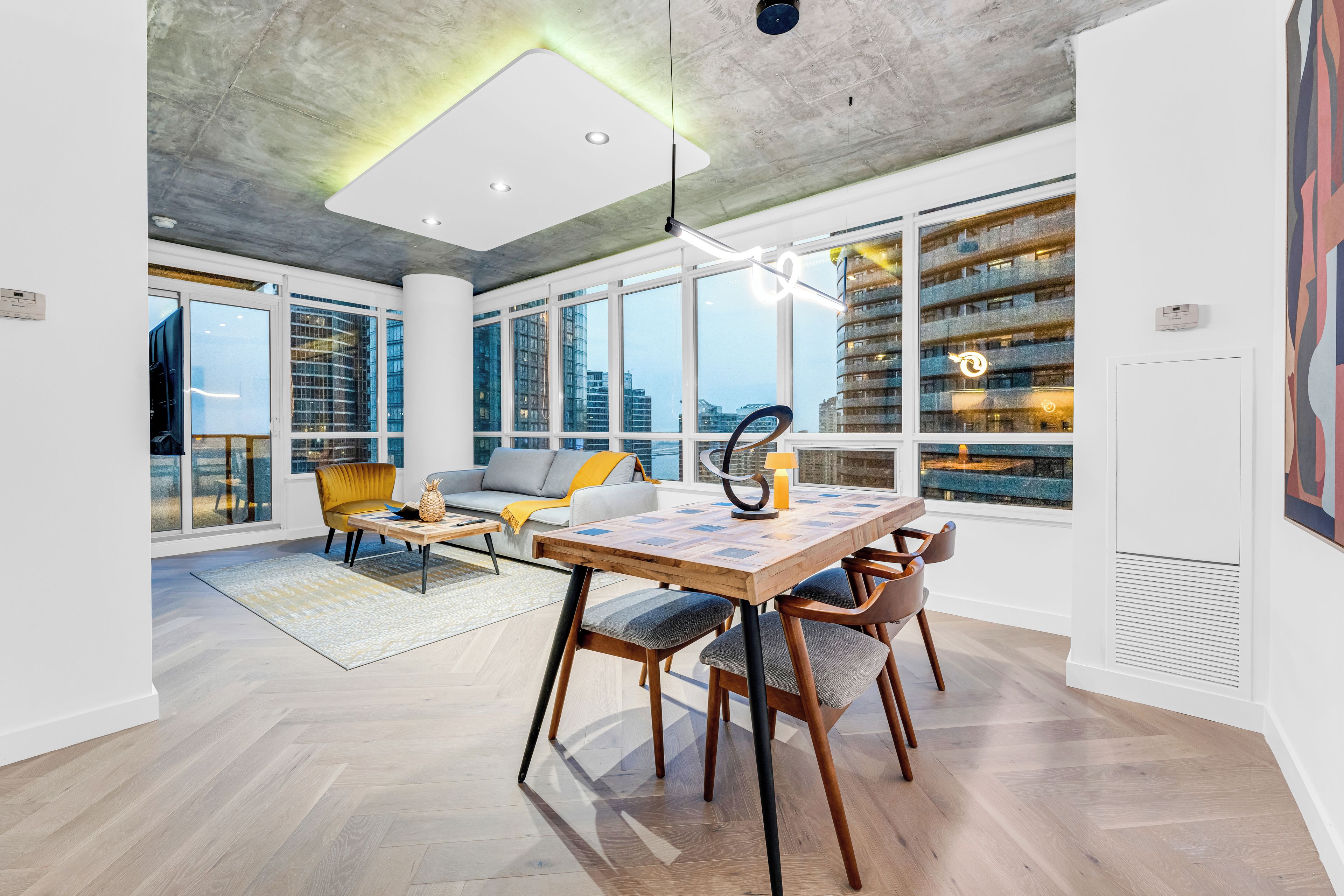A spacious room with a large dining table, comfortable seating, and large windows offering city views.