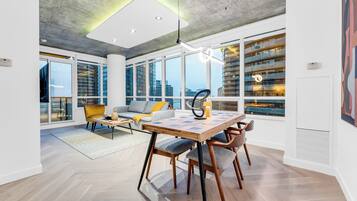 A spacious room with a large dining table, comfortable seating, and large windows offering city views.