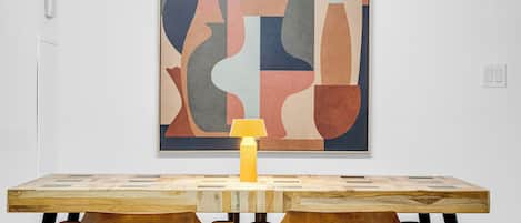 A modern dining area with a wooden table and chairs, a contemporary abstract painting on the wall, and a pendant light above.