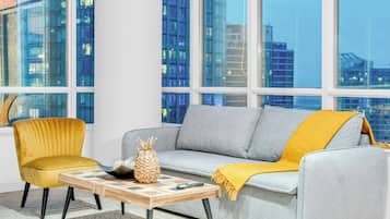 A modern living room with a grey sofa, a yellow armchair, and a wooden coffee table with a pineapple and remote control.