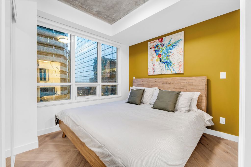 A bedroom with a large bed, a window with multiple panes, and a colorful abstract painting on the wall.
