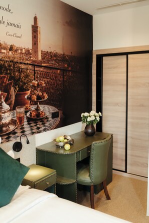 A hotel room with a dining table set for two, a bed, a large poster of a cityscape, and a view of the city through a window. - Art Hotel (Marrakech)