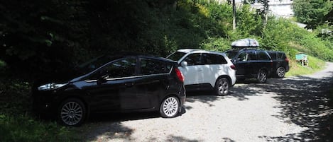 A gravel path with three cars parked on the side, surrounded by greenery and trees.