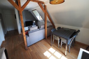 A loft-style room with a wooden beam ceiling, a dining table with chairs, a grey sofa, and a television in the background. - Spacious Half-Timbered Holiday House with Mountain Views for 10 (Schmallenberg)