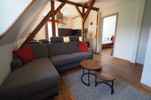 A loft-style living space with a sectional sofa, a small round table, and exposed wooden beams. - Spacious Half-Timbered Holiday House with Mountain Views for 10 (Schmallenberg)