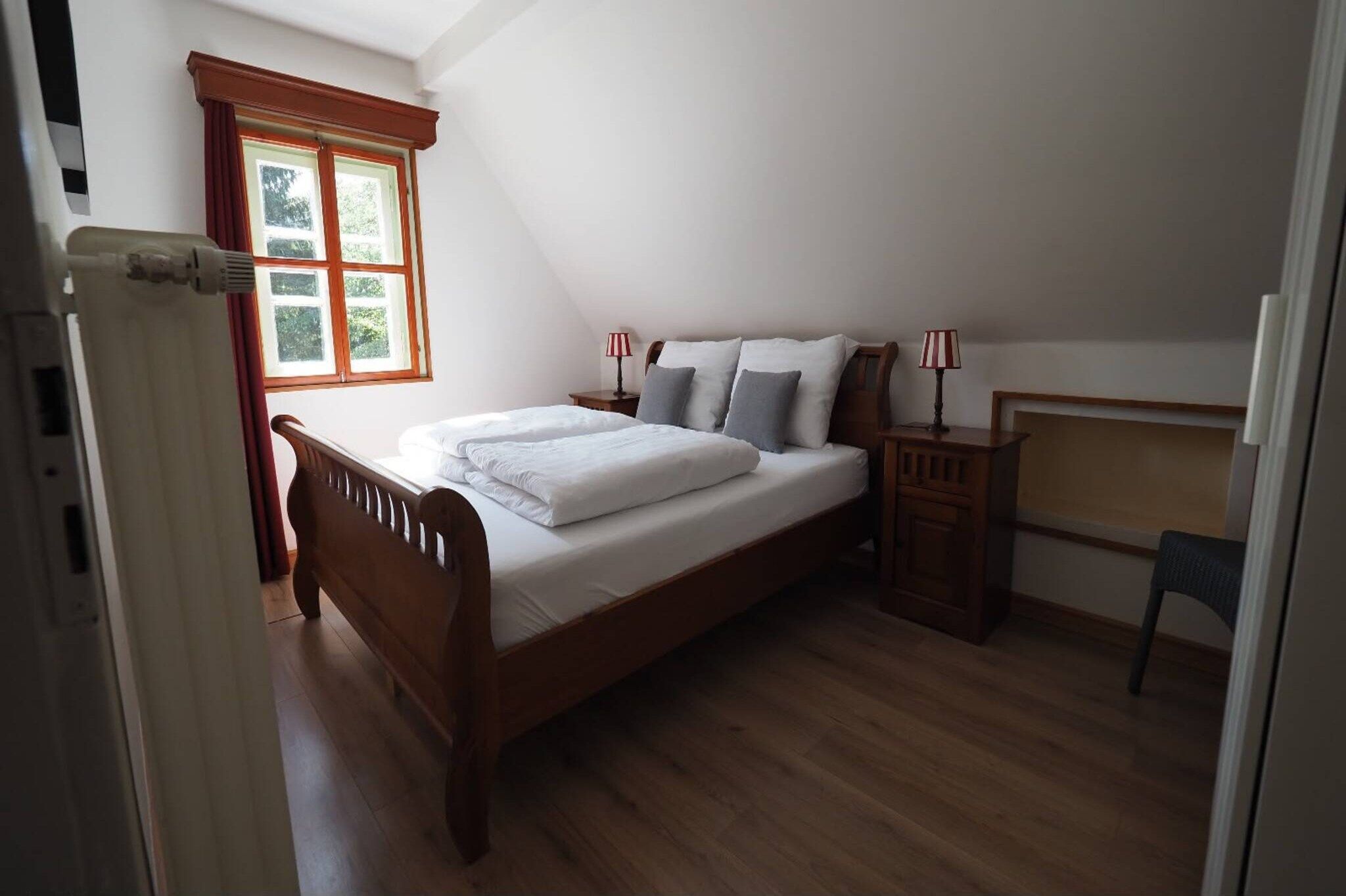 A bedroom with a wooden bed, a nightstand, a chair, and a window with curtains.
